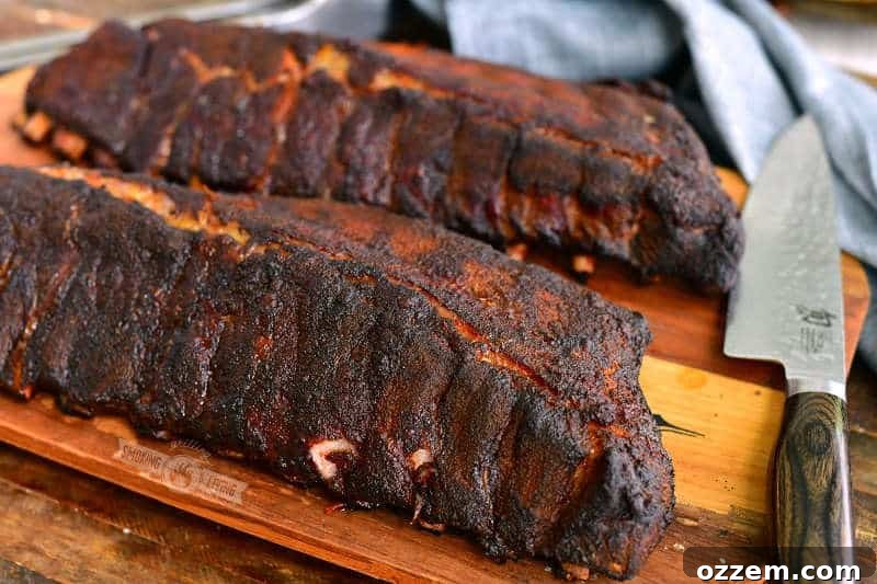 two racks of ribs on the wooden board right off the smoker with a knife and a towel next to it