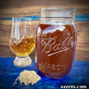 Homemade bourbon bbq sauce in a mason jar with a glass of bourbon and brown sugar.