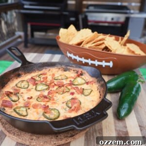 Jalapeno popper dip in a cast iron skillet with a football bowl filled with tortilla chips and two jalapenos.
