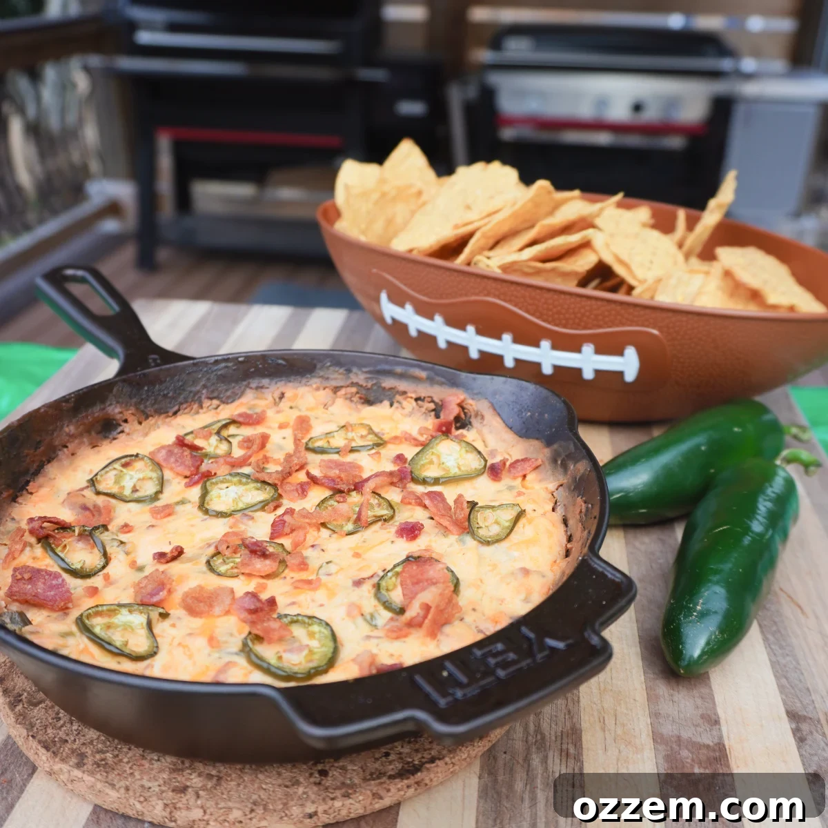Jalapeno popper dip in a cast iron skillet with a football bowl filled with tortilla chips and two jalapenos.