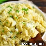 using a wooden spoon to scoop out some potato salad from the white bowl