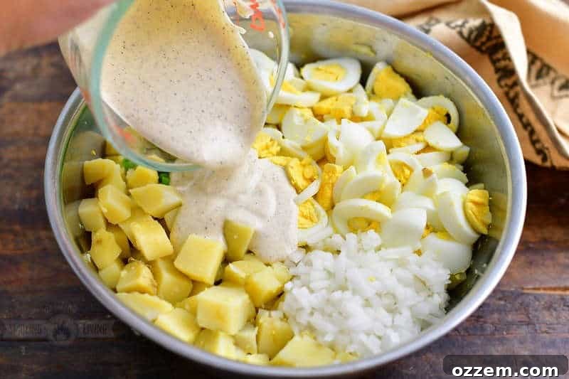 pouring in the mayo mixture over the chopped potatoes, onions, and eggs in a mixing bowl
