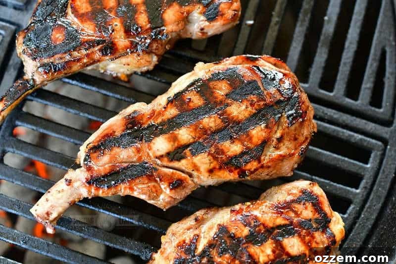 Close-up horizontal view of one grilled pork chop with perfect criss-cross grill marks, flanked by portions of two other pork chops.