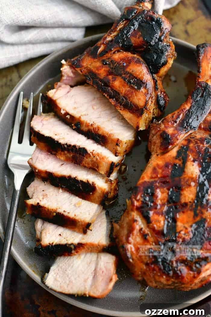 A sliced grilled pork chop presented on a plate next to a whole grilled chop and a fork.