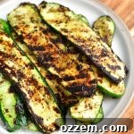 top view of grilled zucchini slices on a plate on to of a wooden cutting board with some brown towel visible