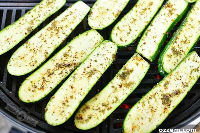 Uncooked, seasoned zucchini slices arranged side-by-side directly on the hot grates of a grill, ready for cooking.