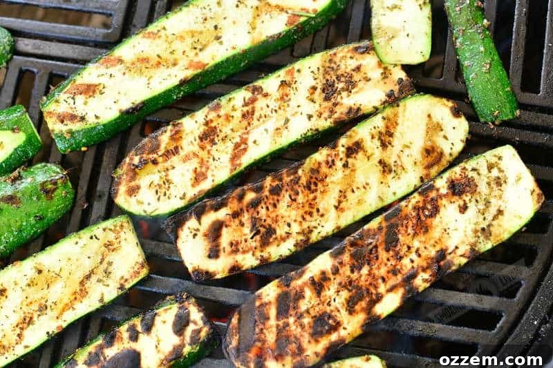 Long slices of perfectly grilled zucchini, displaying beautiful char marks, still hot on the grill grates.