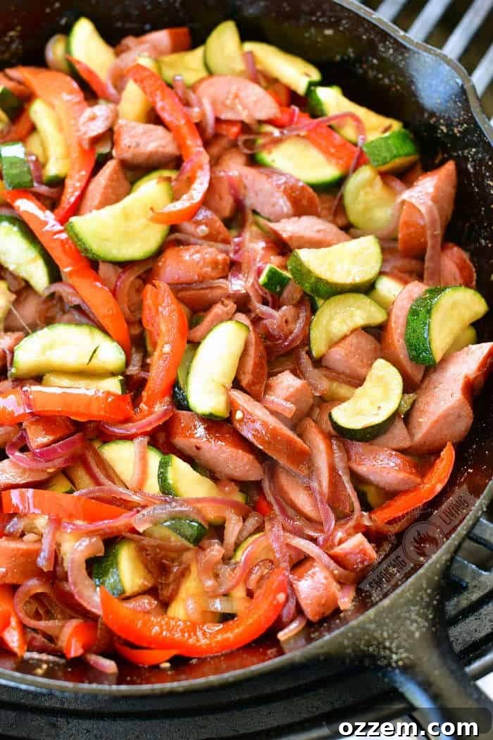 Succulent cooked sausage, vibrant zucchini, caramelized onions, and tender bell peppers sizzling in a cast iron skillet on a hot grill, ready to be served for a delightful outdoor meal.
