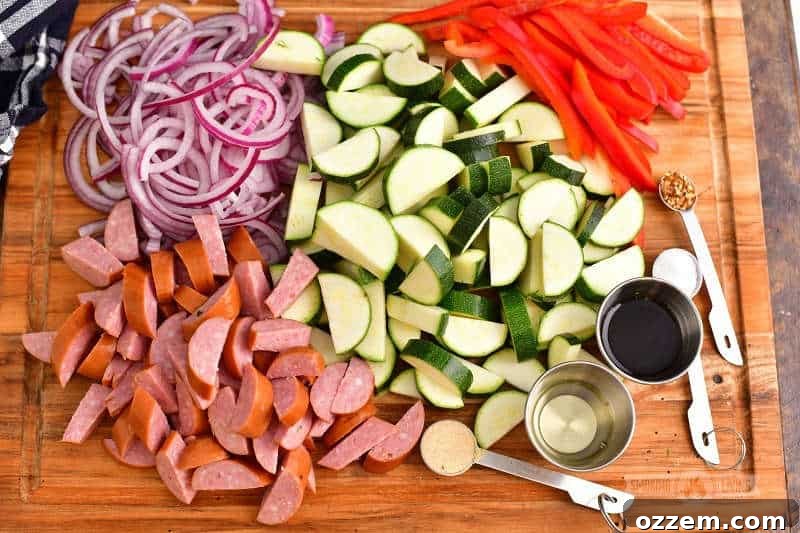 A vibrant flat lay of diced zucchini, pre-sliced smoked sausage, thinly sliced bell pepper, and neatly chopped red onion, accompanied by small silver cups of olive oil and balsamic vinegar, and measuring spoons holding garlic powder, crushed red pepper flakes, and salt, all artfully arranged on a rustic wooden cutting board, showcasing the fresh, prepared ingredients for a grilled meal.