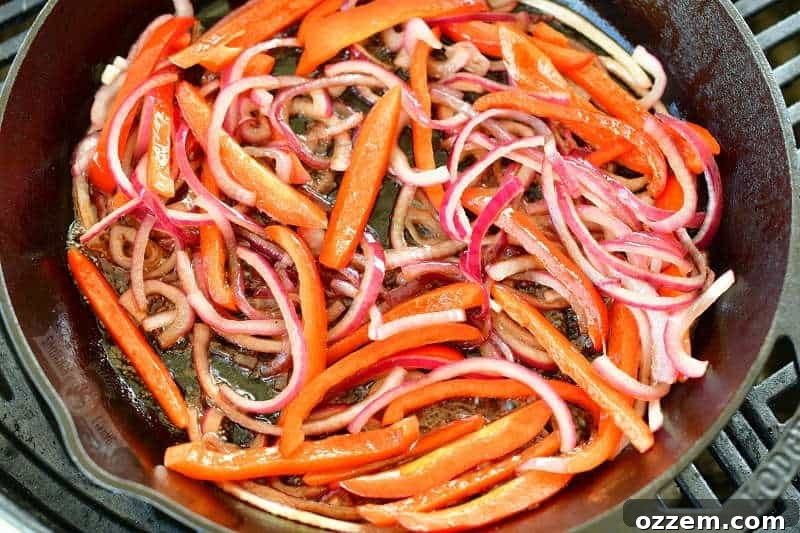 Sliced red onion and vibrant bell pepper sizzling and softening in a hot cast iron skillet on the grill, infused with the rich aroma of balsamic vinegar, a key step in preparing a flavorful grilled dish.