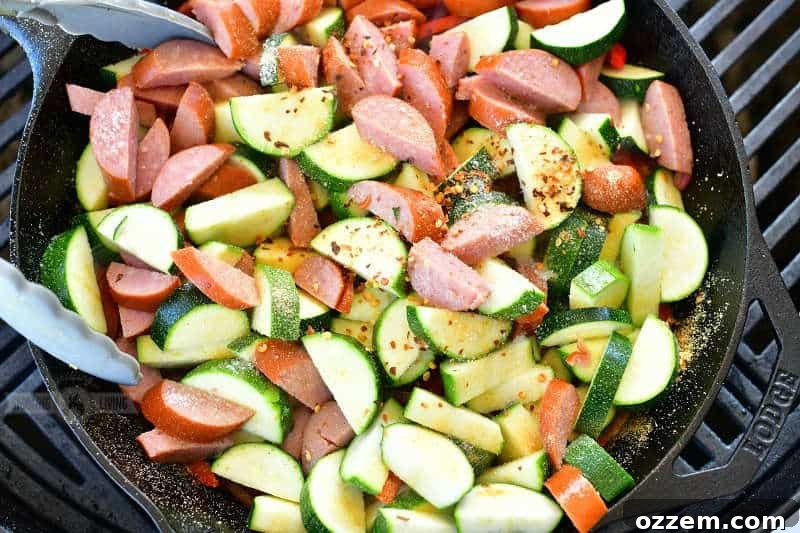 A close-up shot of chopped smoked sausage and vibrant zucchini slices cooking in a cast iron skillet, generously topped with savory garlic powder, a kick of crushed red pepper flakes, and a sprinkle of salt, showcasing the seasoning process for a grilled masterpiece.