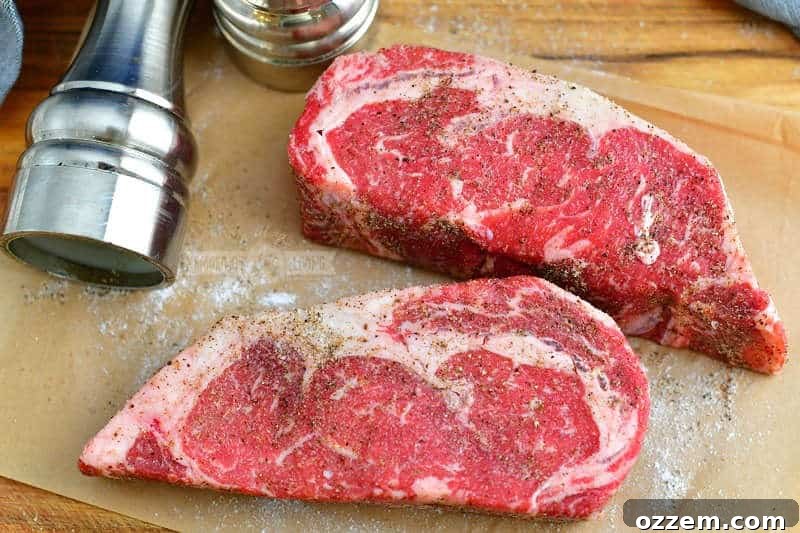 two ribeye steaks seasoned wtih salt and pepper on a cutting board with salt and pepper grinders near