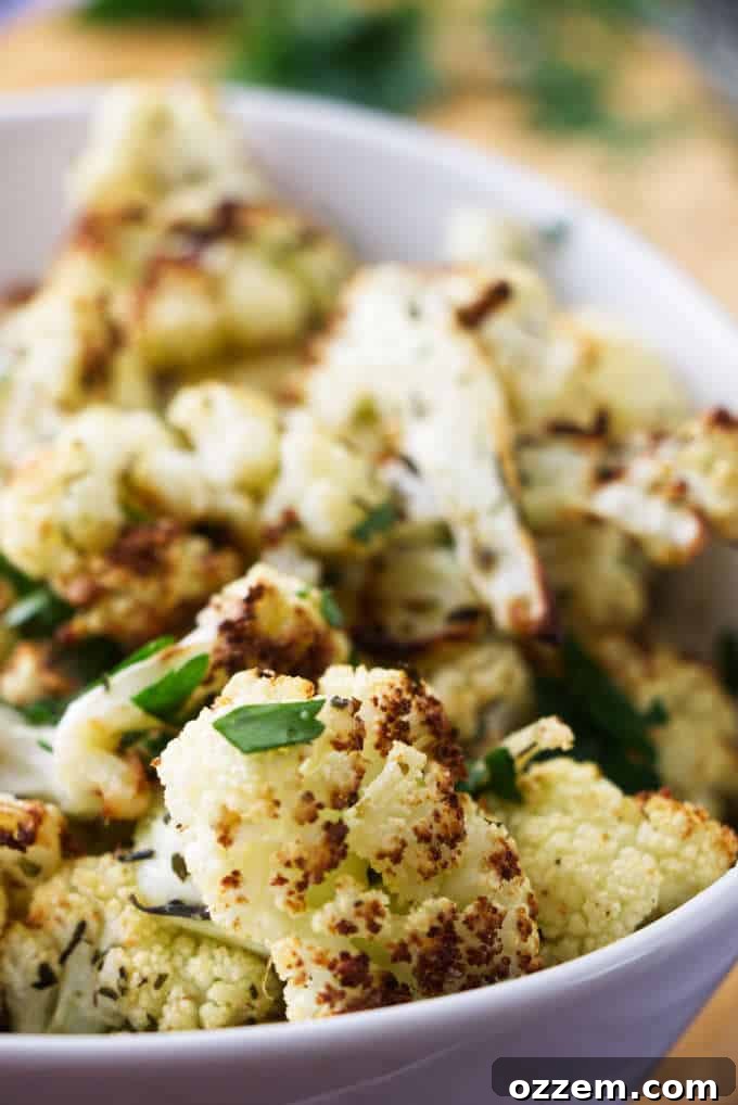 A serving bowl of crispy air fryer cauliflower, garnished with fresh herbs.