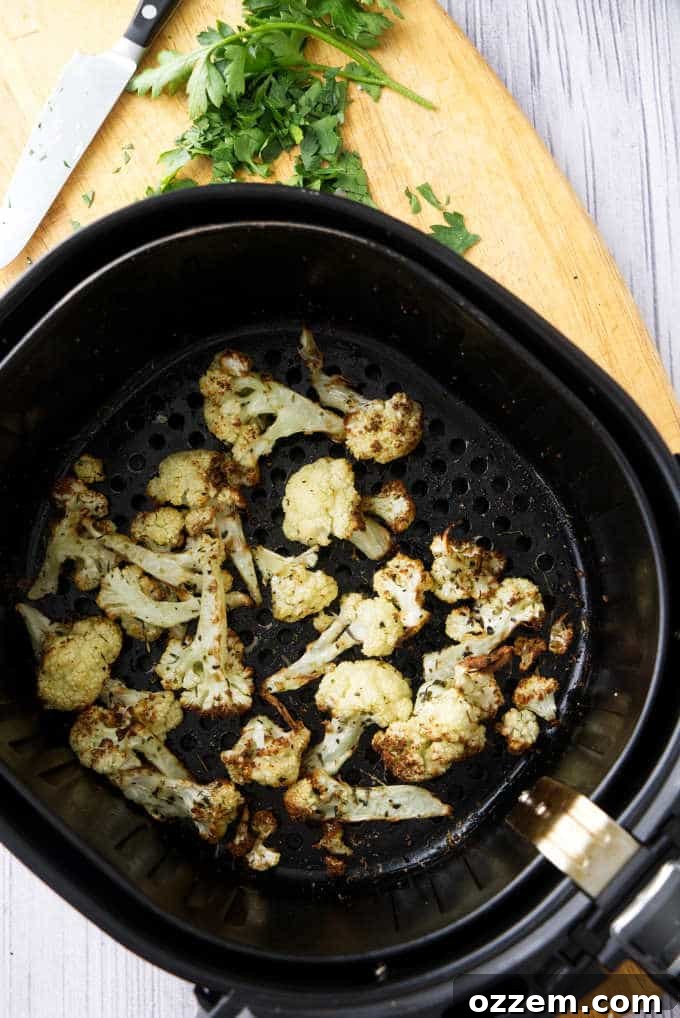 Roasted cauliflower florets cooking in an air fryer basket, showing their golden-brown and crispy texture.