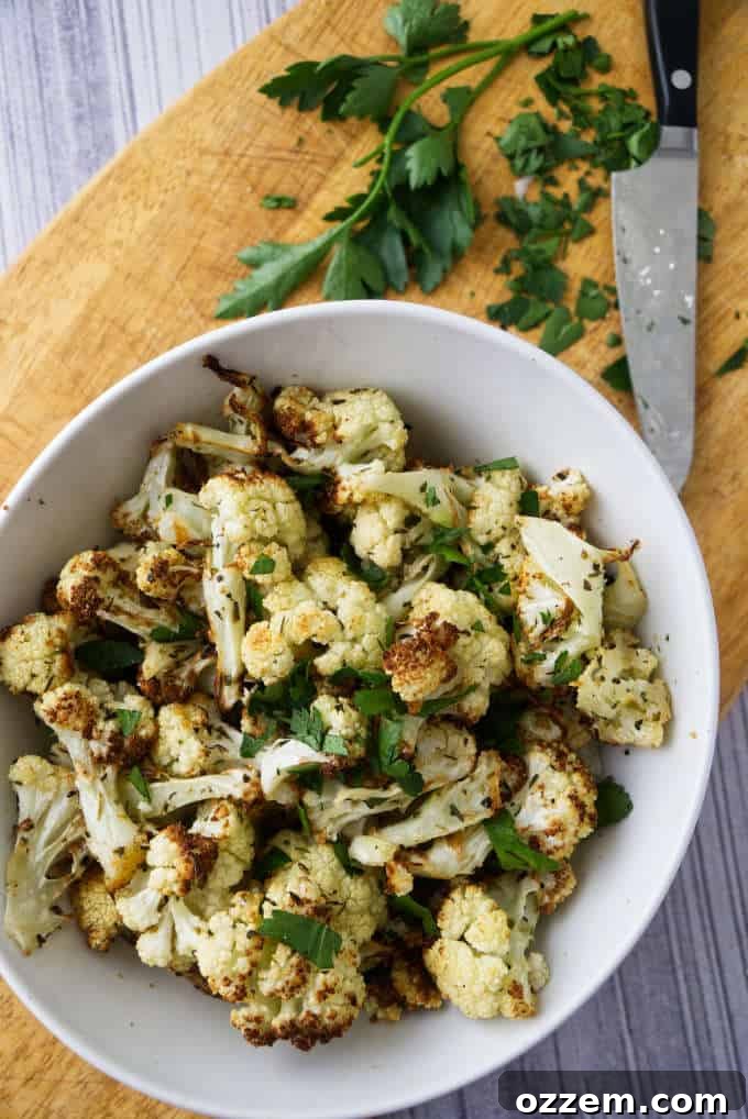 Cauliflower florets in a bowl with fresh parsley on a wooden cutting board, ready for seasoning.