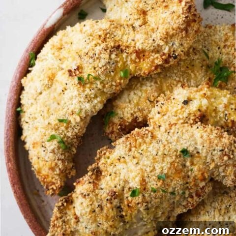 Several air fryer parmesan chicken tenders on a plate with dipping sauce, garnished with fresh herbs.