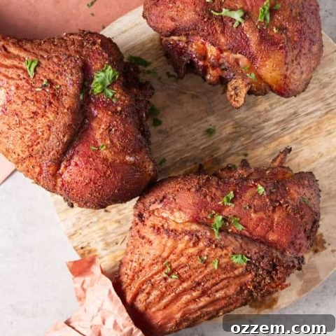 Three smoked turkey legs laying on a concrete table and circular wood cutting board with peach butcher paper