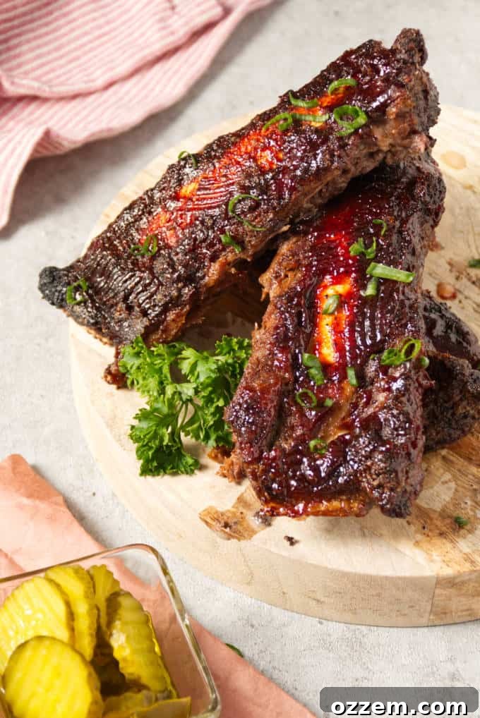 Succulent Air Fryer Beef Ribs 6 Air fryer beef back ribs sliced and coated with BBQ sauce sitting on a butcher block with a side of pickles
