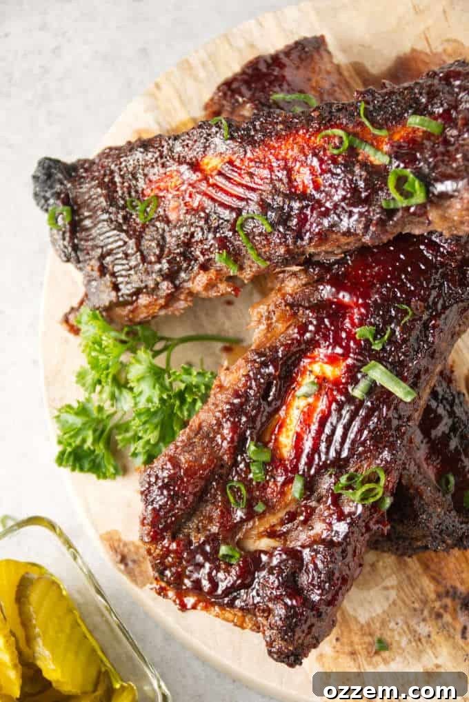 Succulent Air Fryer Beef Ribs 7 Air fryer beef back ribs sliced and coated with BBQ sauce sitting on a butcher block with a side of pickles