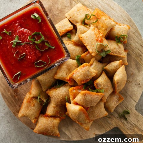 Overhead of pizza rolls stacked on wood cutting board with pizza sauce for dipping.