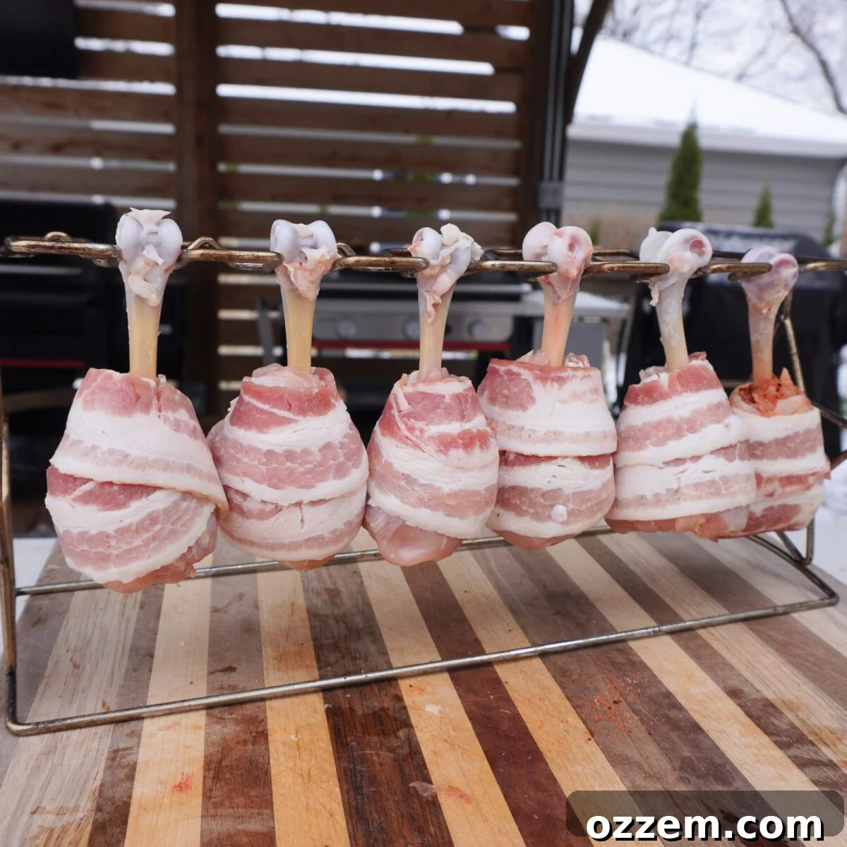 Crispy Bacon Chicken Legs 6 Bacon Wrapped Chicken Drumsticks on a wire rack ready for grilling.