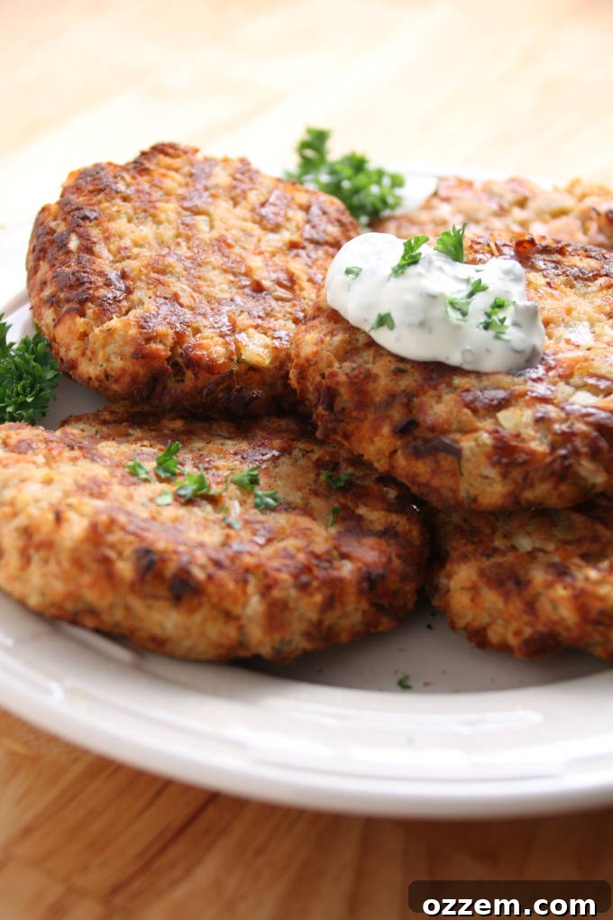 Crispy golden-brown air fryer salmon patties, stacked on a white plate, garnished with a dollop of creamy tartar sauce and fresh dill.
