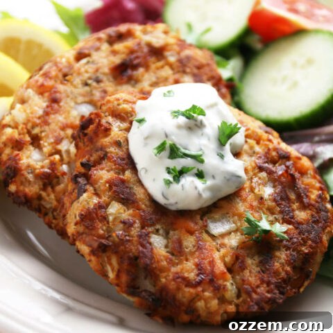 Golden brown salmon cakes with a dollop of tartar sauce on top, presented beautifully on a plate with a fresh garden salad, ready to be served.