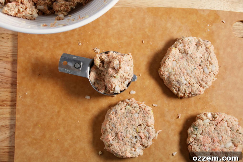 A measuring cup being used to scoop and form air fryer salmon patty mixture into uniform shapes on a cutting board.