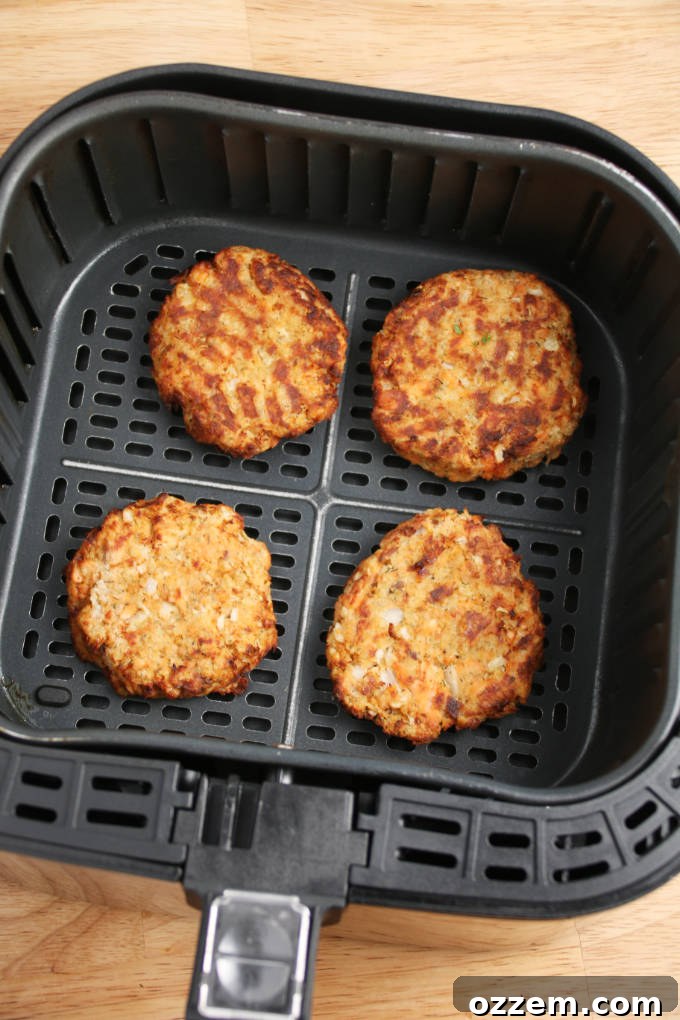 Two perfectly cooked, golden-brown salmon cakes resting in an air fryer basket, highlighting their crispy texture.