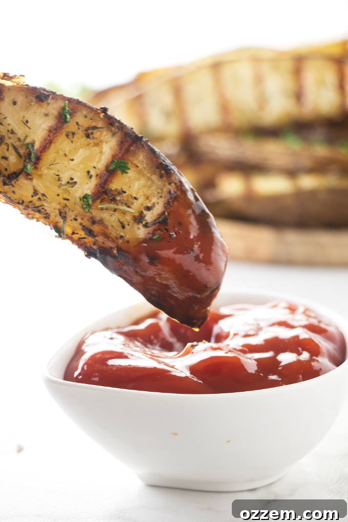 Crispy grilled potato wedges being dipped into a dollop of vibrant red ketchup, showcasing their golden-brown exterior and perfect grill marks.