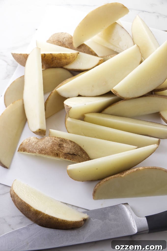 A hand expertly slicing a raw potato into uniform 1/2-inch thick wedges on a wooden cutting board.