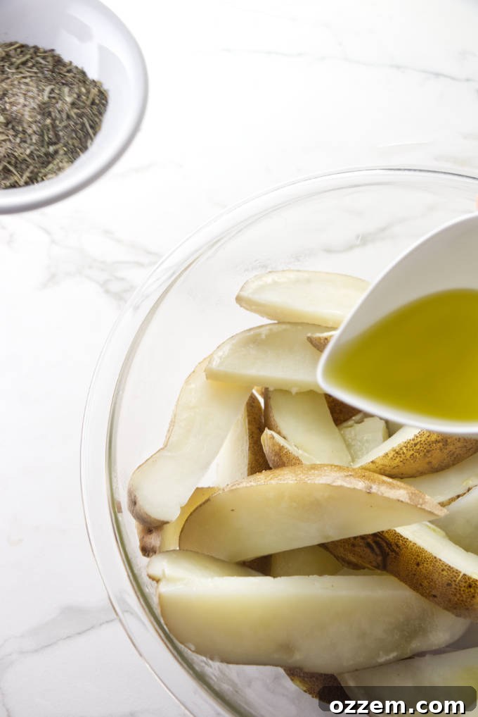 Close-up of potato wedges being tossed in a large metal bowl with olive oil and a mixture of dried herbs and spices.