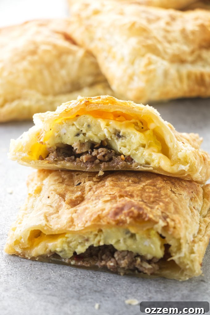 A freshly baked, golden brown air fryer breakfast pocket cut in half to showcase its delectable filling of scrambled eggs, crumbled sausage, and melted cheese.