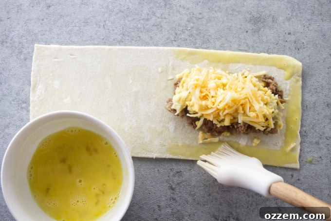 Applying an egg wash to the edges of a puff pastry strip to help seal the breakfast pocket.