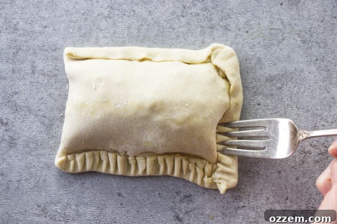 Using a fork to crimp and press down the edges of a breakfast pocket, ensuring a tight seal.