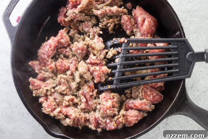 Ground sausage cooking and browning in a hot skillet, being broken up with a spatula.
