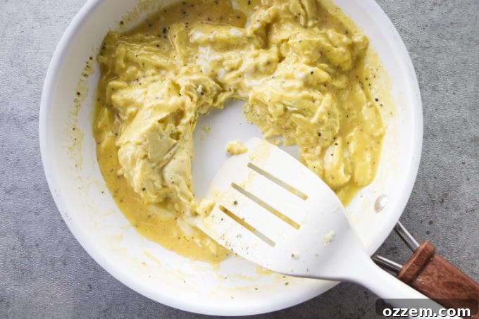 Fluffy scrambled eggs cooking gently in a skillet, stirred occasionally.