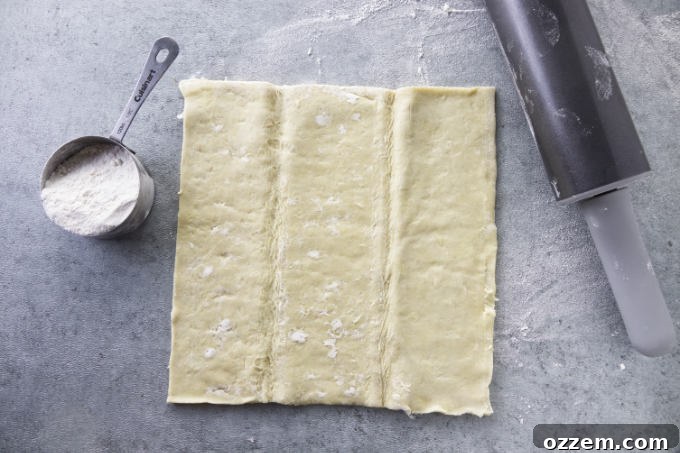 A sheet of puff pastry laid out on a floured counter with a rolling pin nearby, ready for preparation.