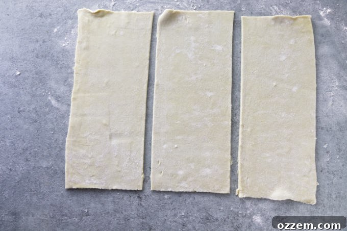 A puff pastry sheet being sliced into three uniform rectangles with a sharp knife.