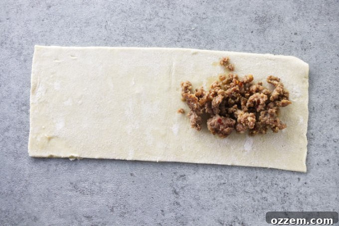A small mound of cooked sausage carefully placed on one half of a pastry strip, leaving space around the edges.