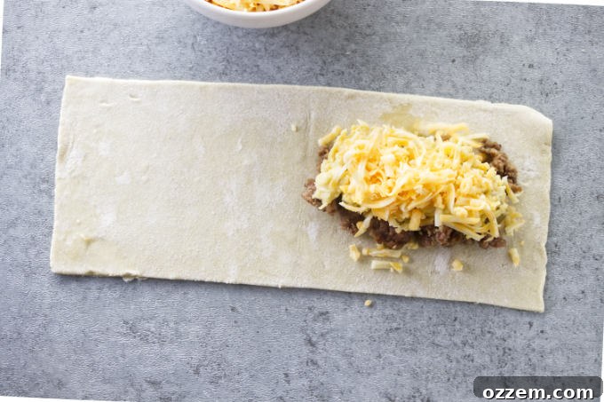 The remaining breakfast pocket filling, including scrambled eggs and shredded cheese, being added on top of the sausage.