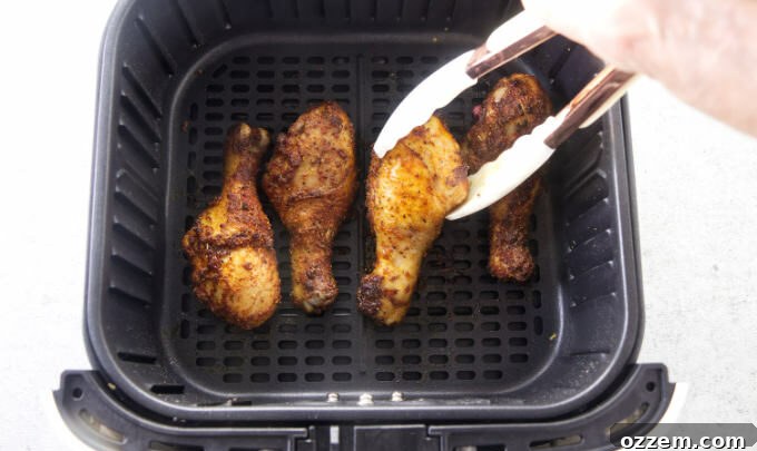Placing drumsticks into an air fryer basket.
