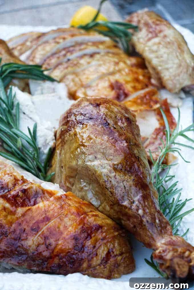 Close up of a carved turkey on a serving platter with fresh herbs, ready for the holiday table.