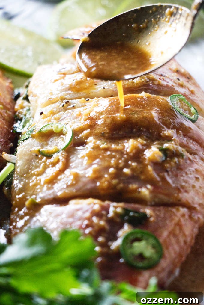 A whole tilapia is generously drizzled with the vibrant chili-lime sauce, preparing it for grilling.