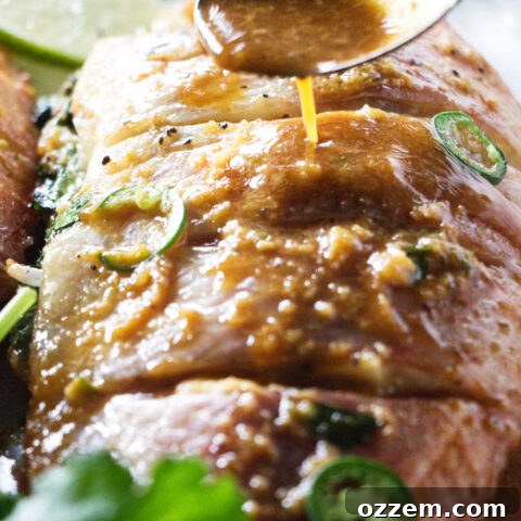 Grilled whole tilapia being drizzled with chili-lime sauce on a rustic serving board.