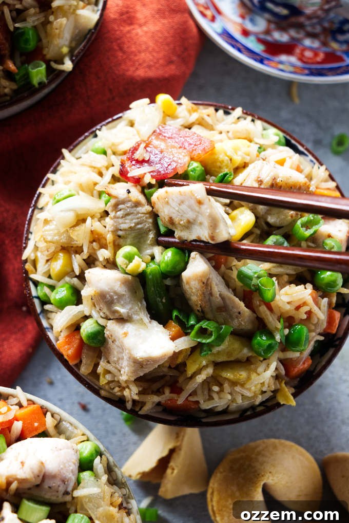 Chopsticks picking up a piece of chicken from a bowl of fried rice.