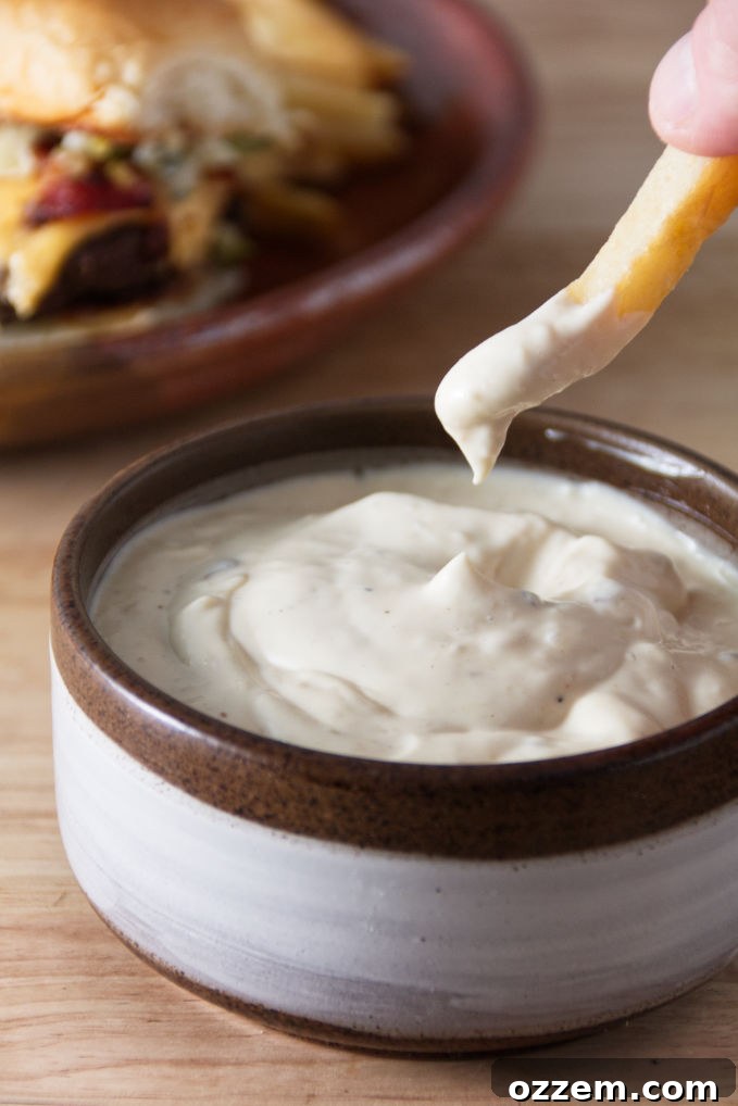 A close-up shot of creamy, golden Donkey Sauce in a ceramic bowl, with a perfectly cooked golden french fry being dipped into it, ready for a delicious bite.
