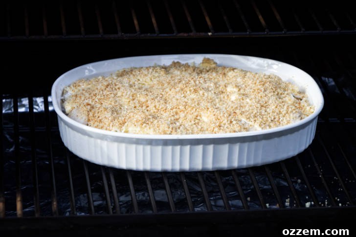 A casserole dish of au gratin potatoes cooking inside a Traeger pellet grill, showing the golden-brown top and bubbling sauce.