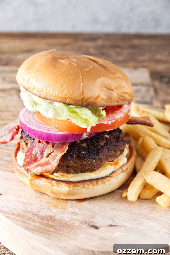 burger with bacon, onion, tomato, lettuce, and donkey sauce sitting on cutting board with fries