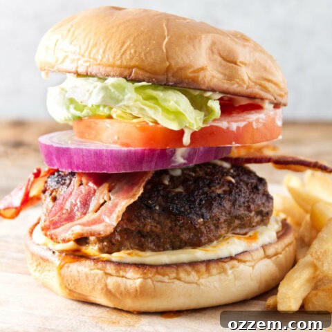 burger with bacon, onion, tomato, lettuce, and donkey sauce sitting on cutting board with fries